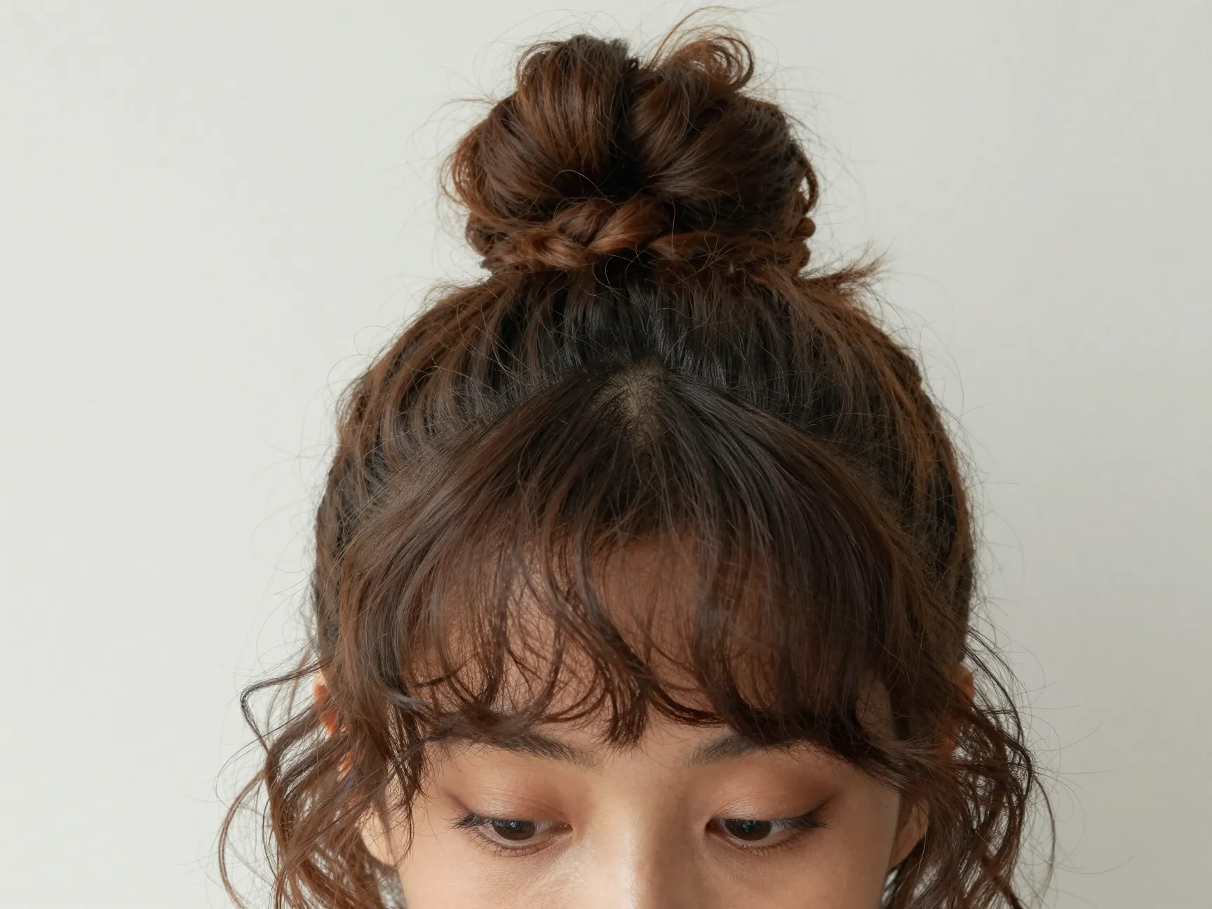 A high bun at the crown with a curly fringe falling across the forehead
