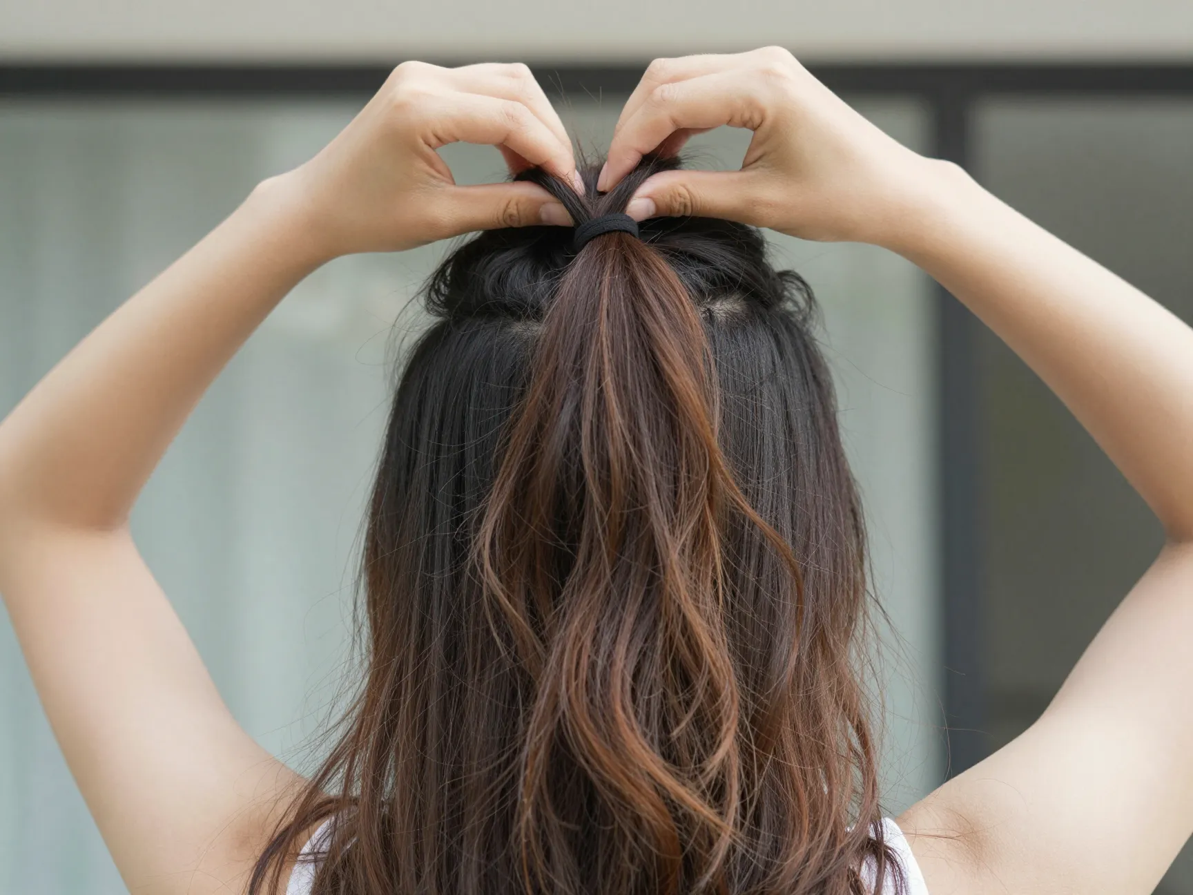 A woman securing the top half of her hair at the crown