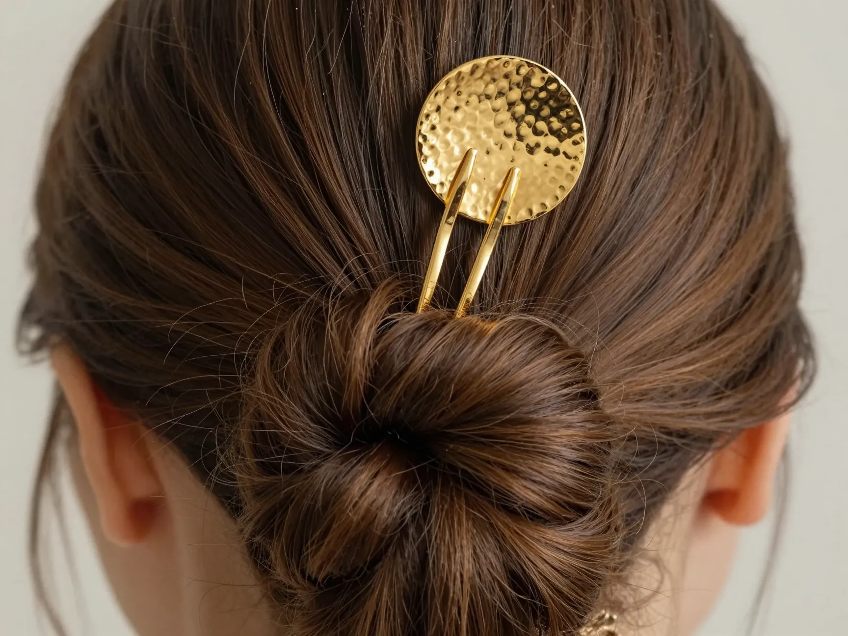 Two prong gold hair fork with disc topper securing a thick bun
