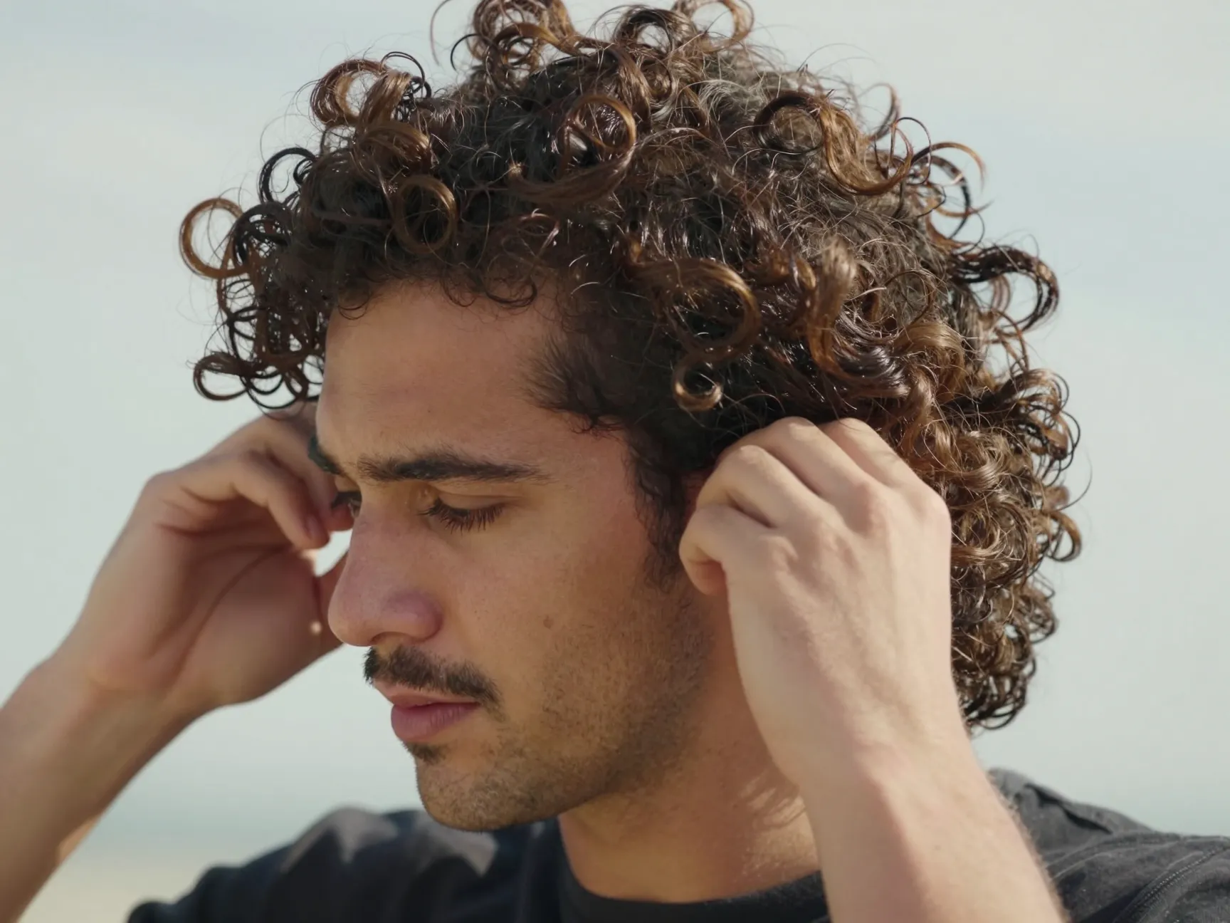 A man with curly flow hair tucks strands behind his ears