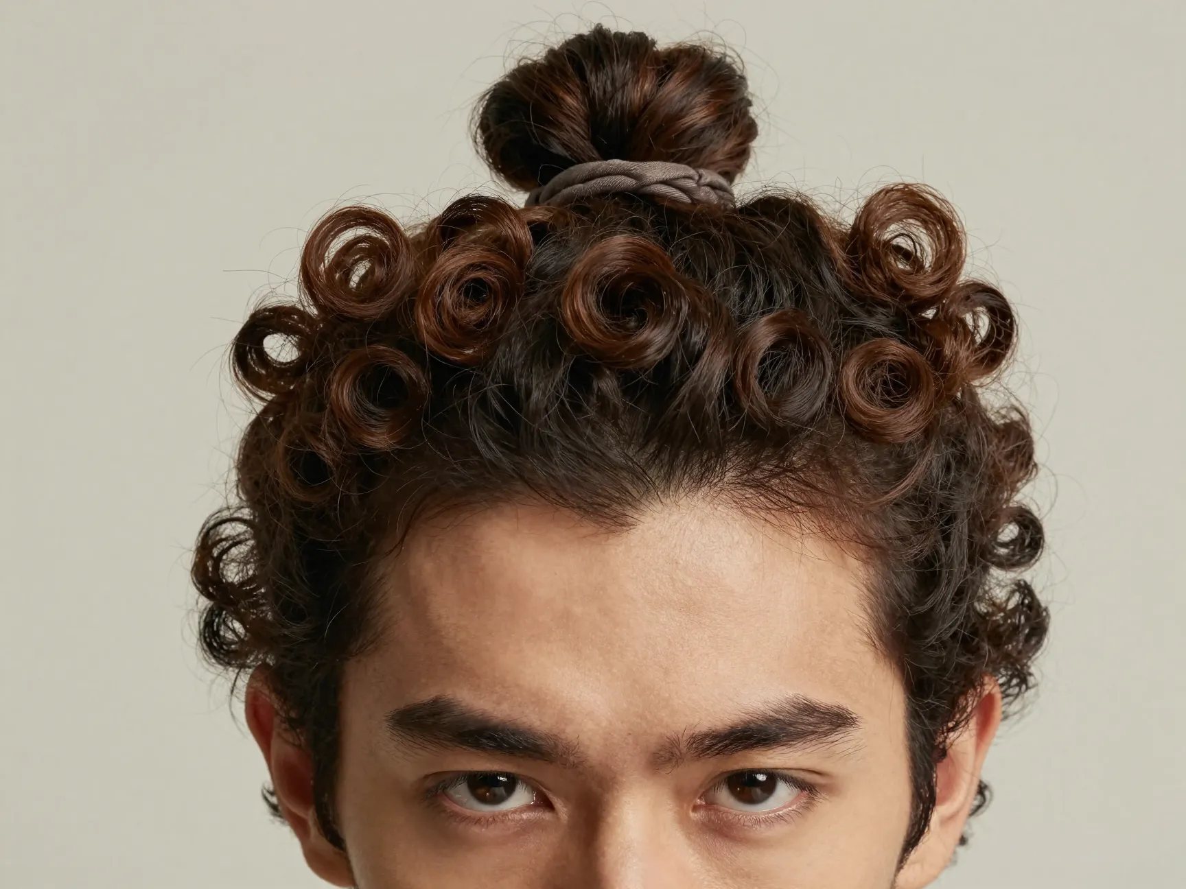 Polished curly bun on a man at the crown with face framing curls